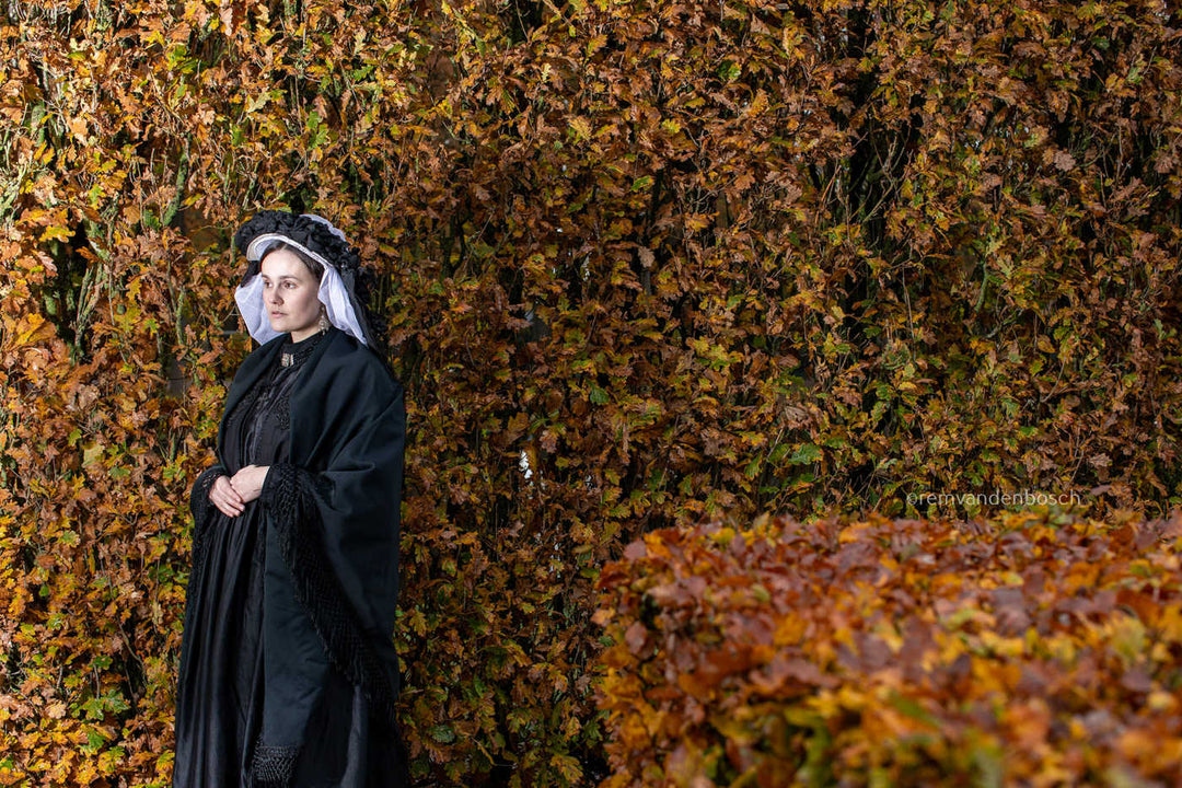 Liggend portret van Linde in traditionele Limburgse dracht voor een herfstige haag, dromerig wegkijkend. Fotografie Rem van den Bosch 