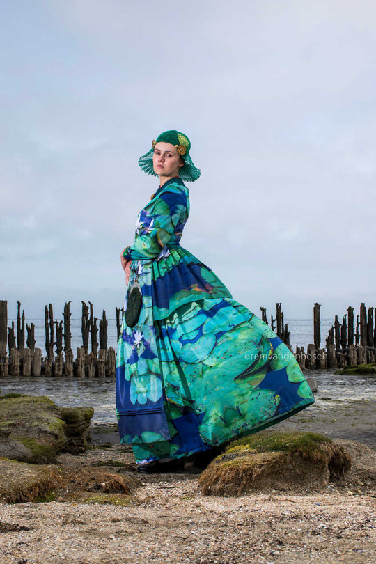 Linde in moderne groene Friese dracht met waterlelieprint in zijaanzicht tussen paalhoofden met wind in de rok