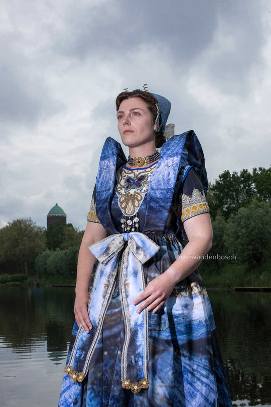 Staand portret van Janis in moderne Axelse dracht in blauwtinten met watertoren van Axel , fotografie door Rem van den Bosch
