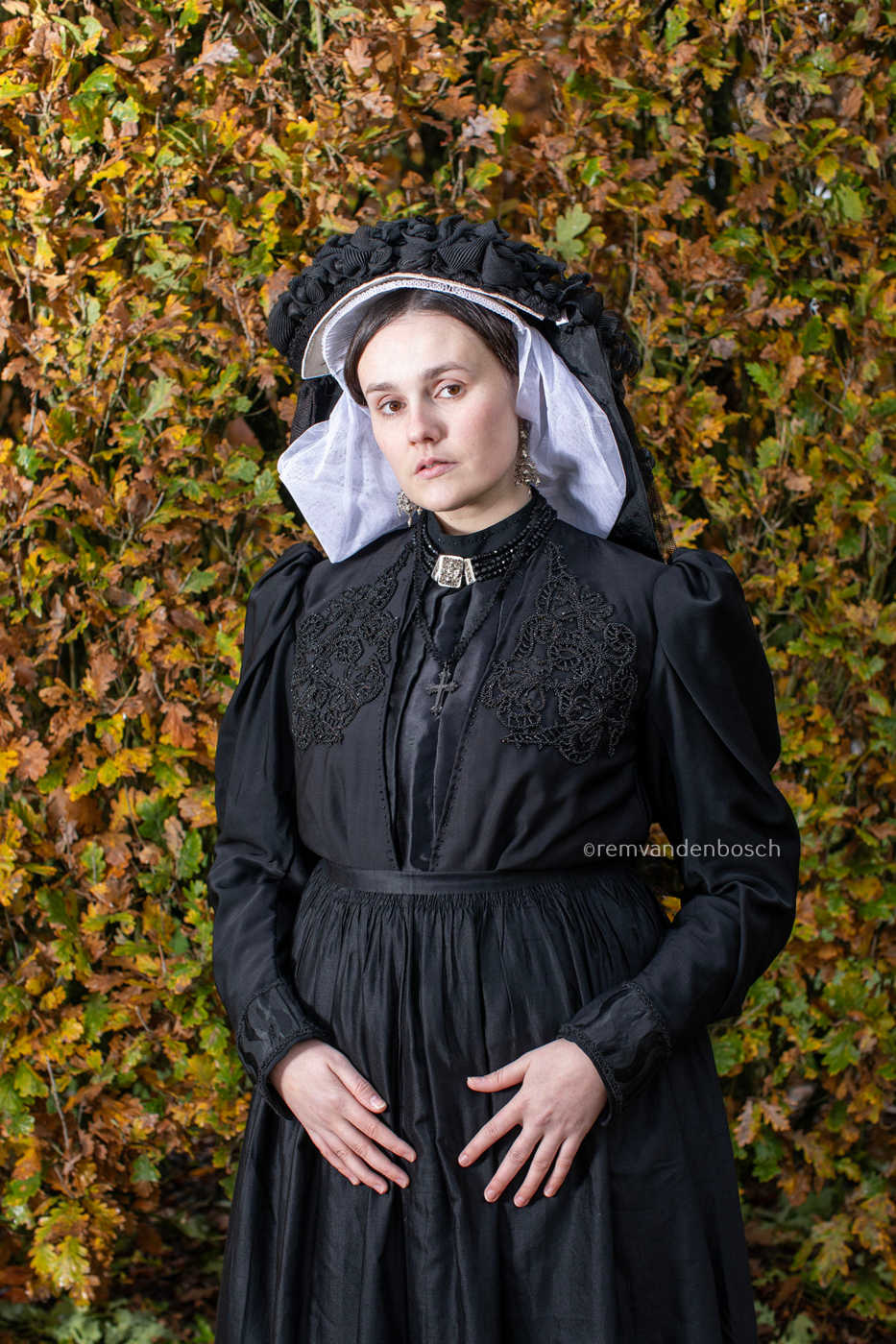 Staand portret van Linde in traditionele Limburgse dracht met dromerige blik voor een herfstige haag. Fotografie Rem van den Bosch 