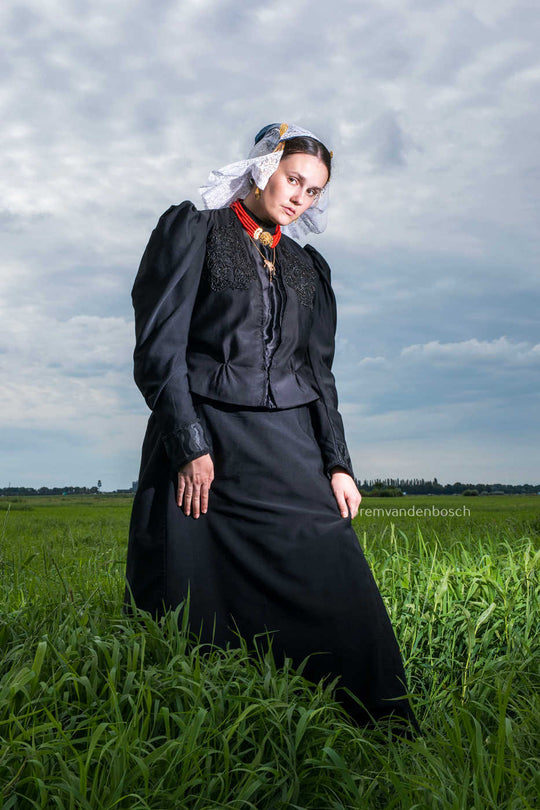 Linde in traditionele dracht van Gooi- en Eemland, staand in een veld en de kijker aankijkend. Fotografie Rem van den Bosch 