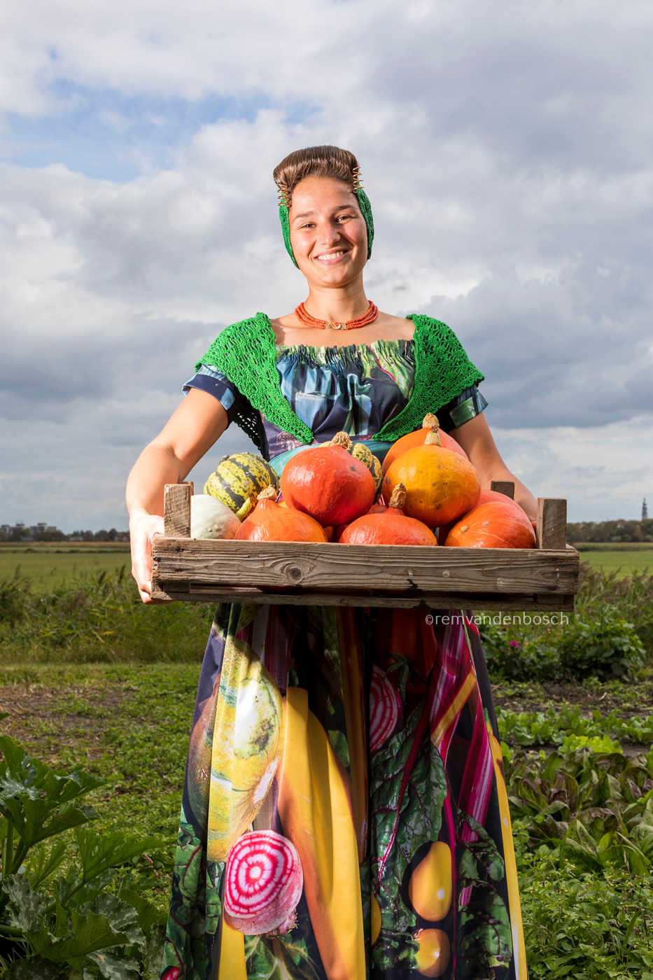 Joyce in moderne Walcherse groentendracht, lachend in het veld met een houten krat vol pompoenen ,Zeeuwse wandkunst