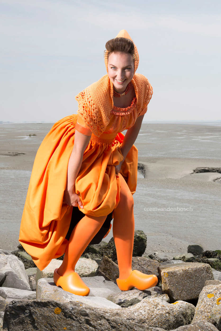Ruby in moderne oranje Walcherse dracht op de dijk, blij en ondeugend kijkend in de camera , Zeeuwse wandkunst