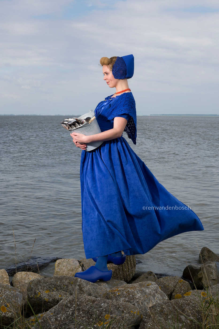 Wahine in moderne Walcherse dracht op rotsen aan zee met een emmer vis, Zeeuwse wandkunst