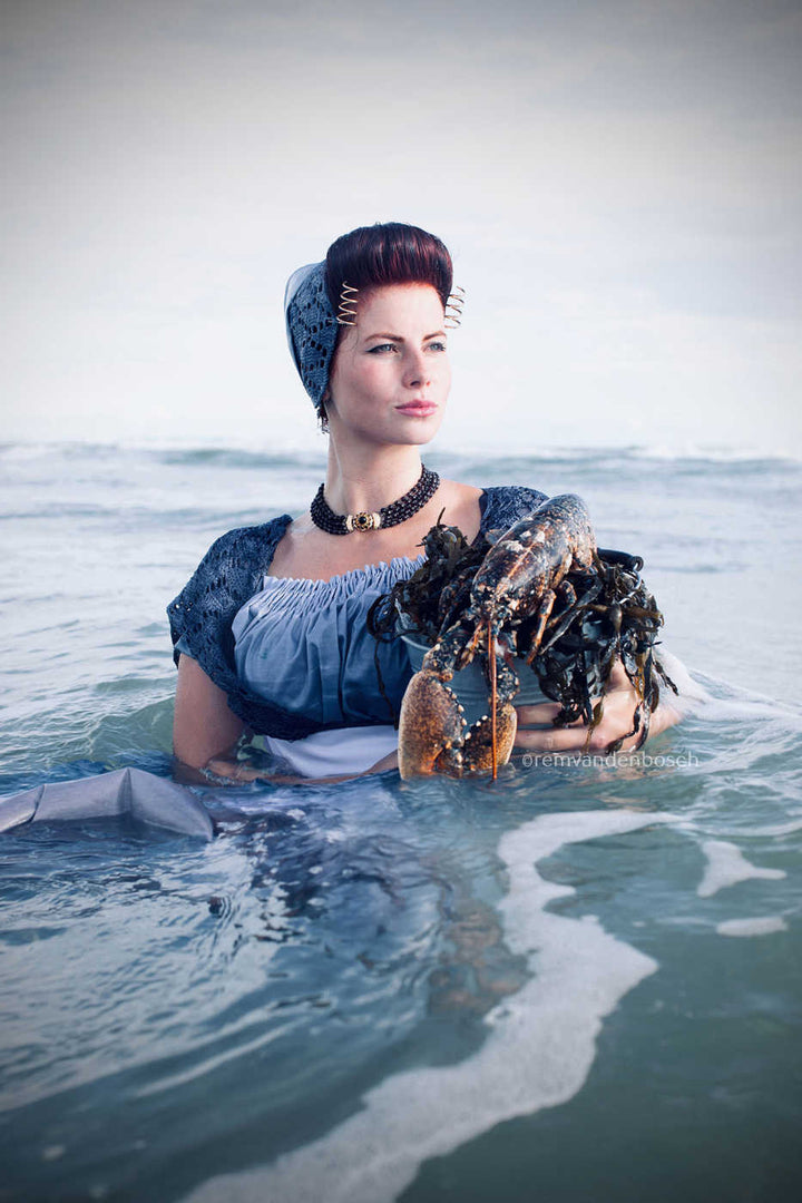 Staand fotobeeld van Eline in moderne blauwe Walcherse dracht met kreeft in het water, fotografie Rem van de Bosch 