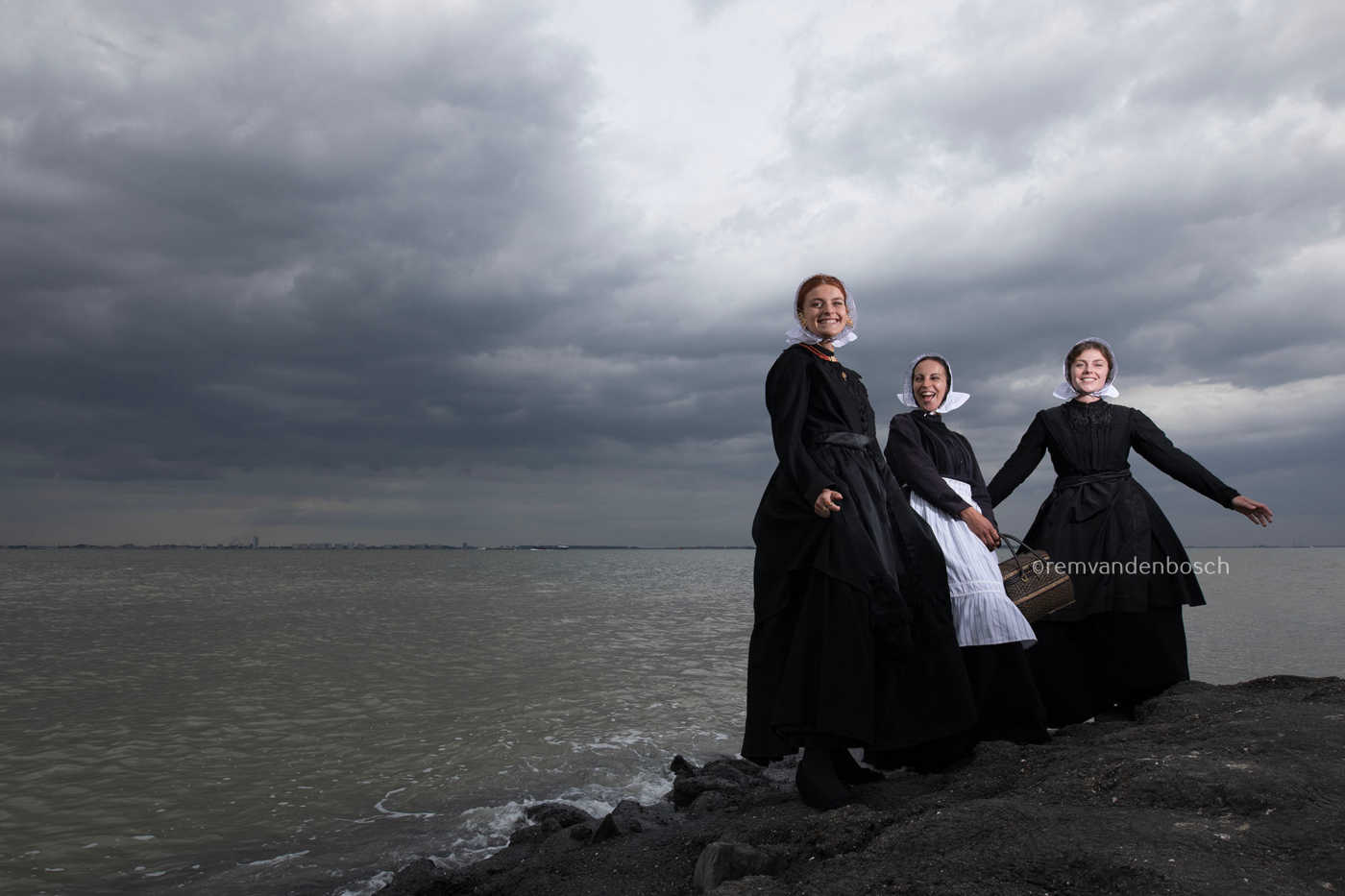 Liggend portret van Charlotte, Janis en Ilyana in Cadzandse dracht aan zee, stralend en vrolijk, kunstfotografie door Rem van den Bosch