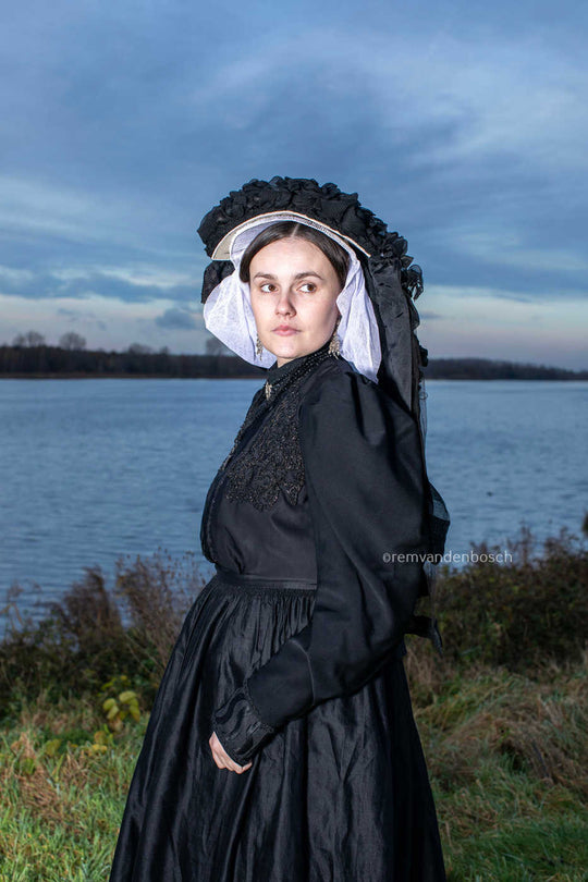 Staand portret van Linde in de dracht van Limburg aan het water met een schuin afgewende blik, tijdloze Nederlandse wandkunst. Fotografie Rem van den Bosch 