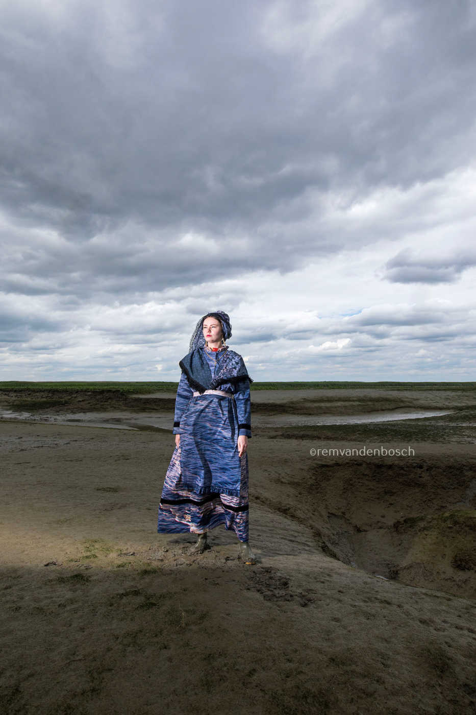 Staand portret van Lois in moderne Hulster dracht in blauw-grijze tinten in Saeftinghe, kunstfotografie door Rem van den Bosch