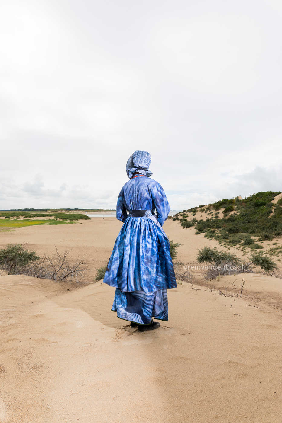 Rugaanzicht van Jazzmine in moderne Cadzandse dracht in blauwtinten in de duinen, kunstfotografie door Rem van den Bosch