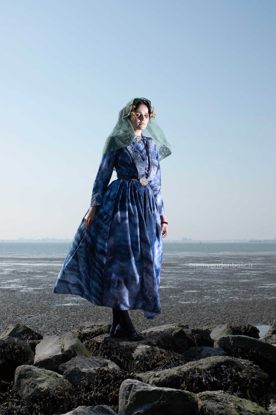 Portret van Linde in de moderne blauwe Thoolse dracht aan zee op de rotsen. Verkrijgbaar op dibond of plexiglas via Zeeuwsmeisje.nu