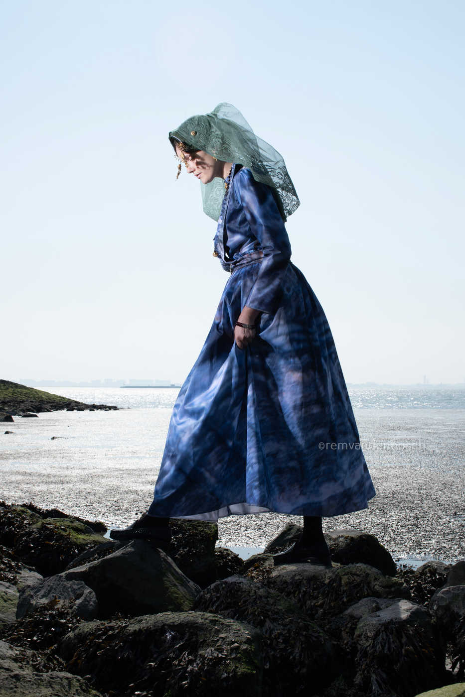 Portret van Linde in de moderne Thoolse dracht aan zee terwijl zij loopt over rotsen. 